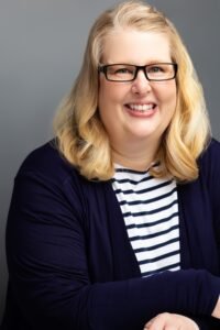 Headshot of Natalie MacLees, a middle age white woman wearing glasses and a navy blue blazer.